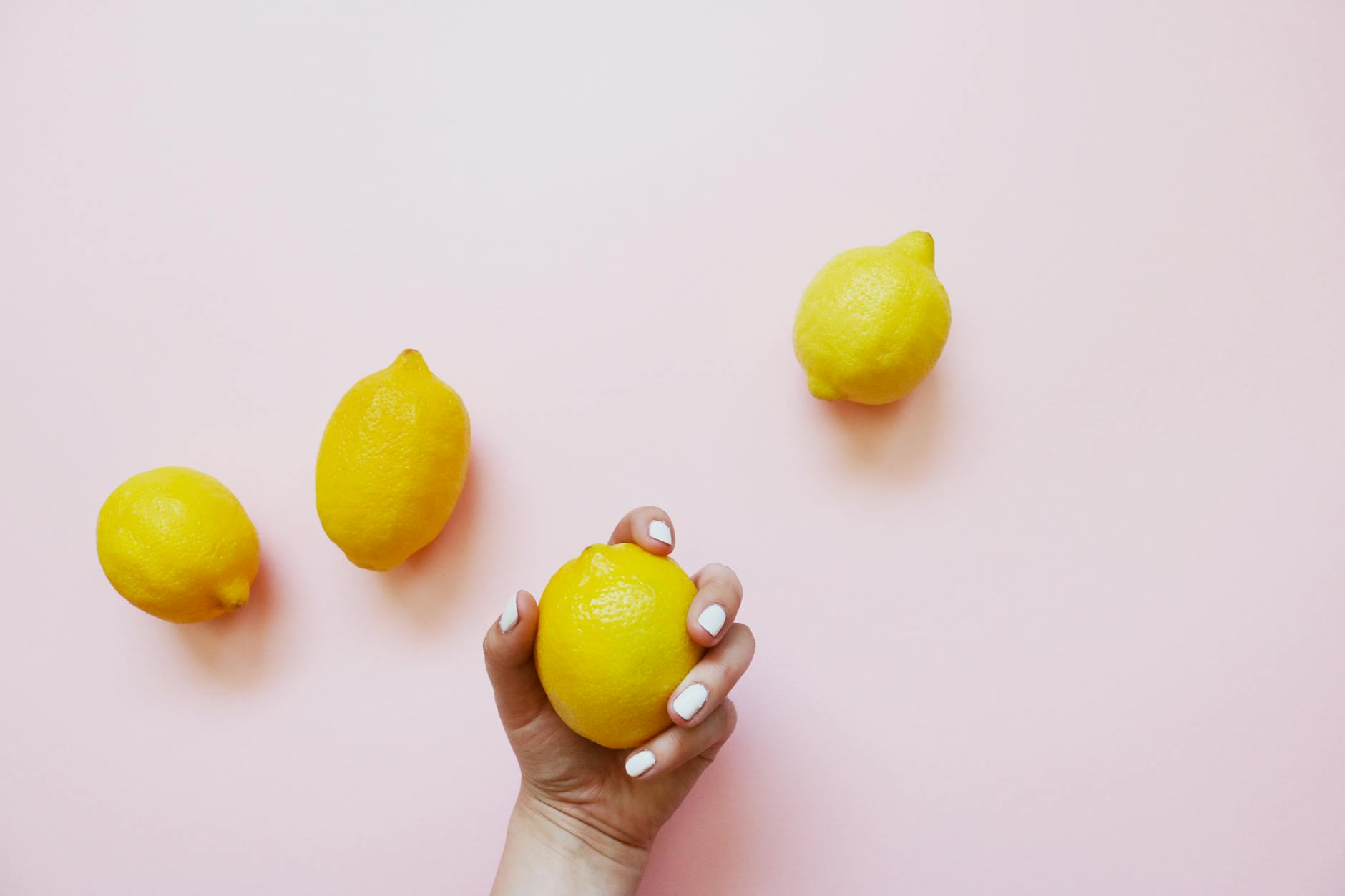 A hand holding a fresh lemon on a soft pink background, symbolizing renewed pleasure and vitality