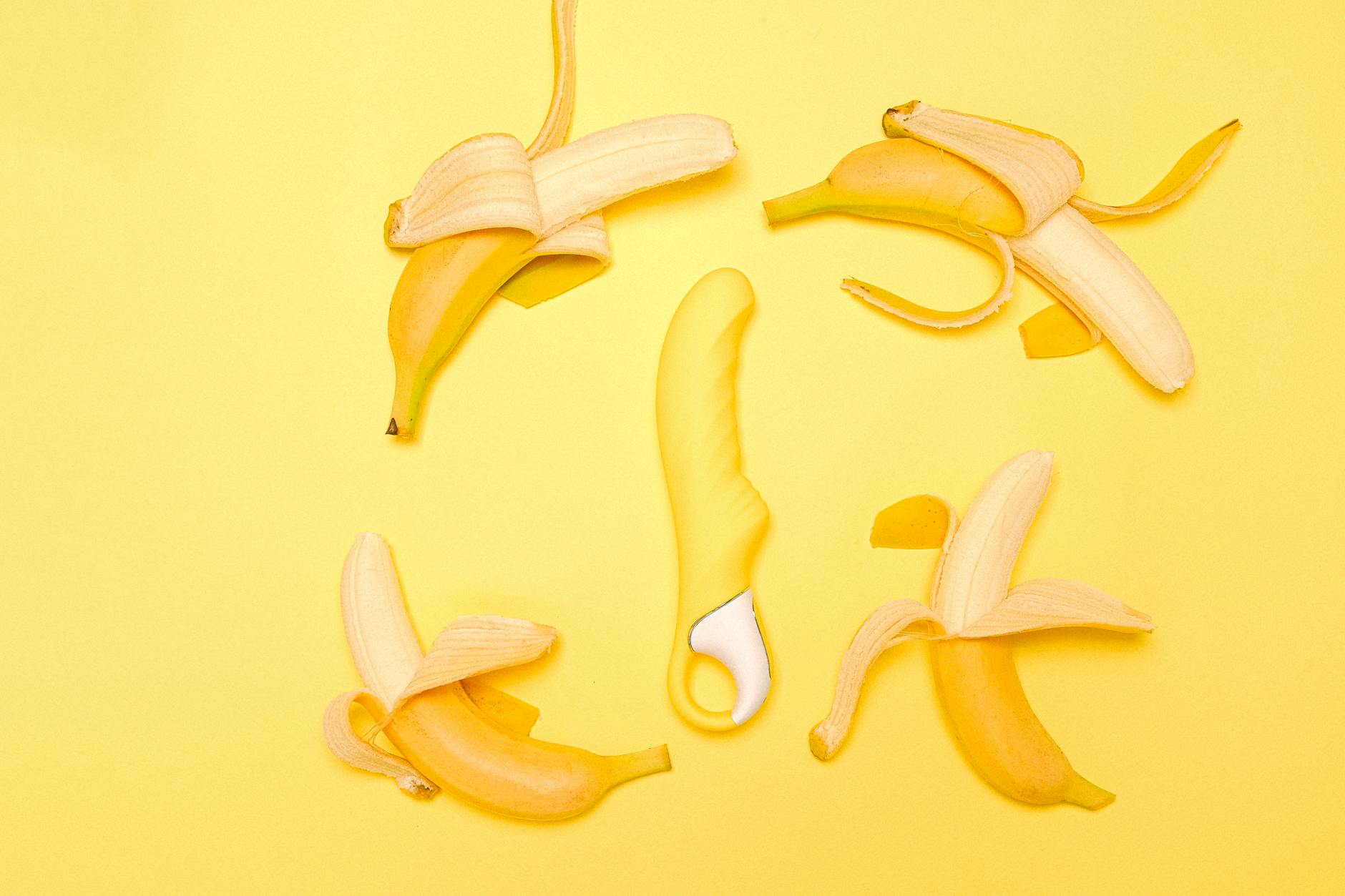 A bright yellow silicone lemon vibrator surrounded by fresh peeled bananas on a yellow background