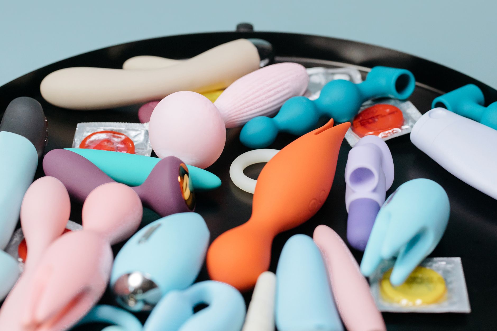 A vibrant collection of various intimate wellness devices on a black tray, featuring diverse shapes and colors.