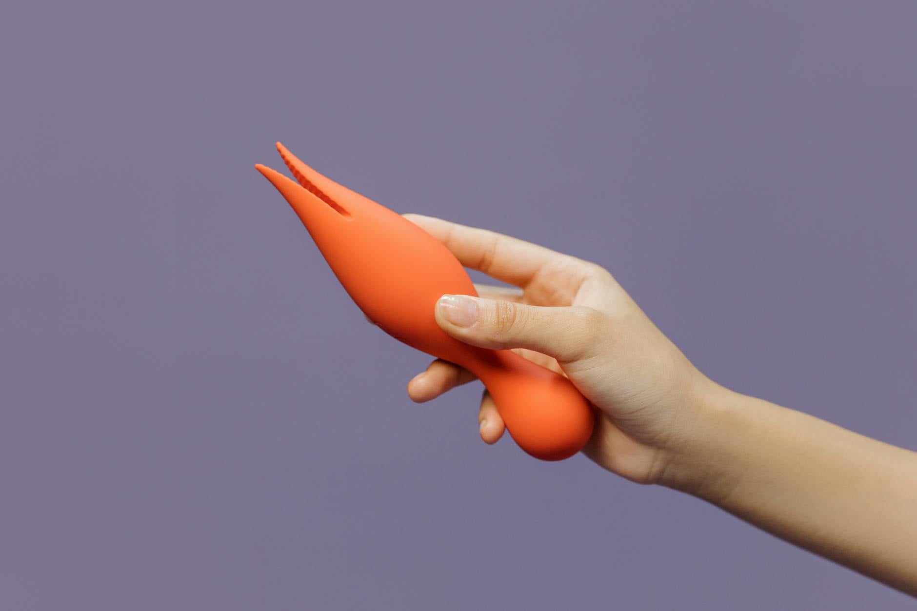 Close-up of a hand holding a lemon clitoral vibrator against a purple backdrop