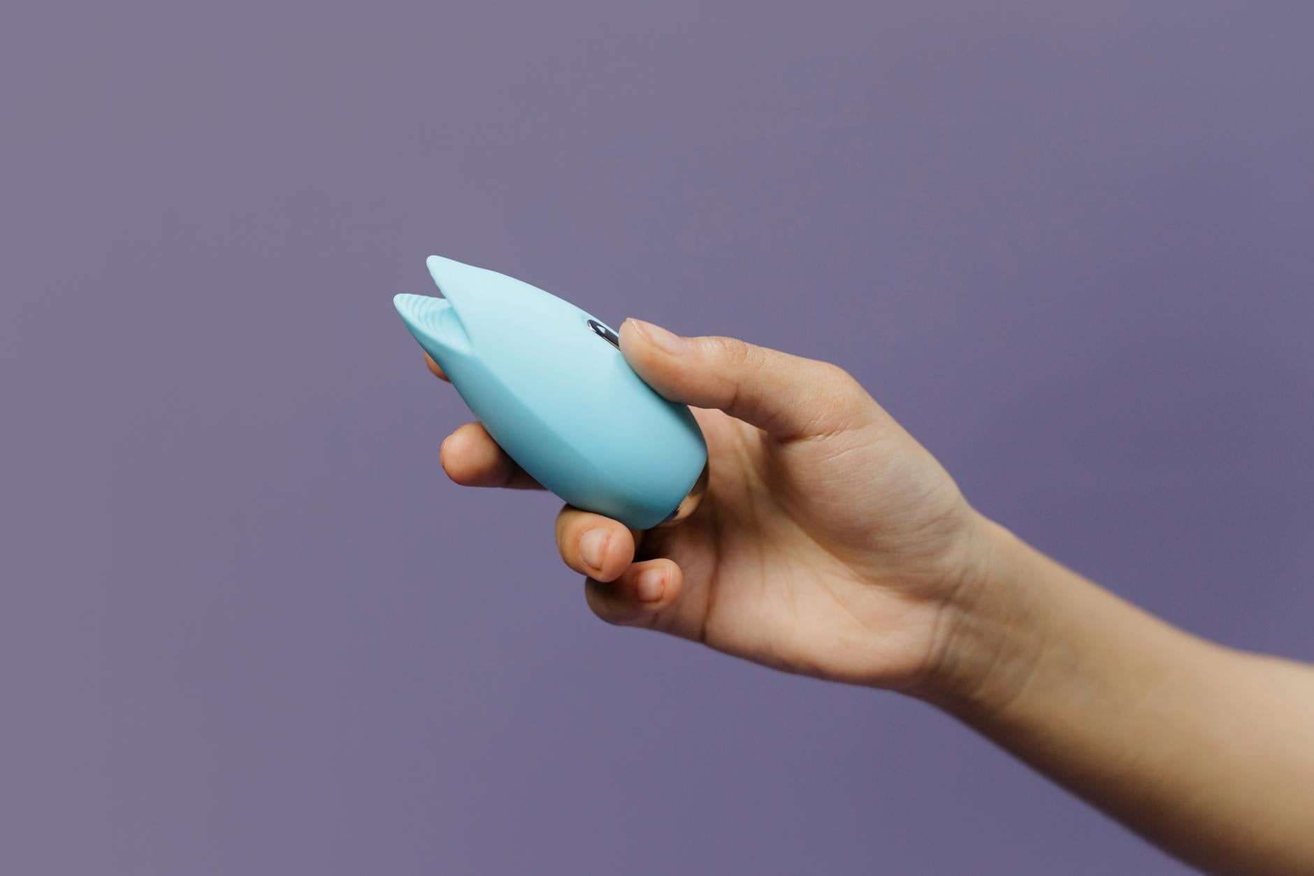 A silicone clitoral vibrator held in hand against a solid background, showcasing modern lemon design