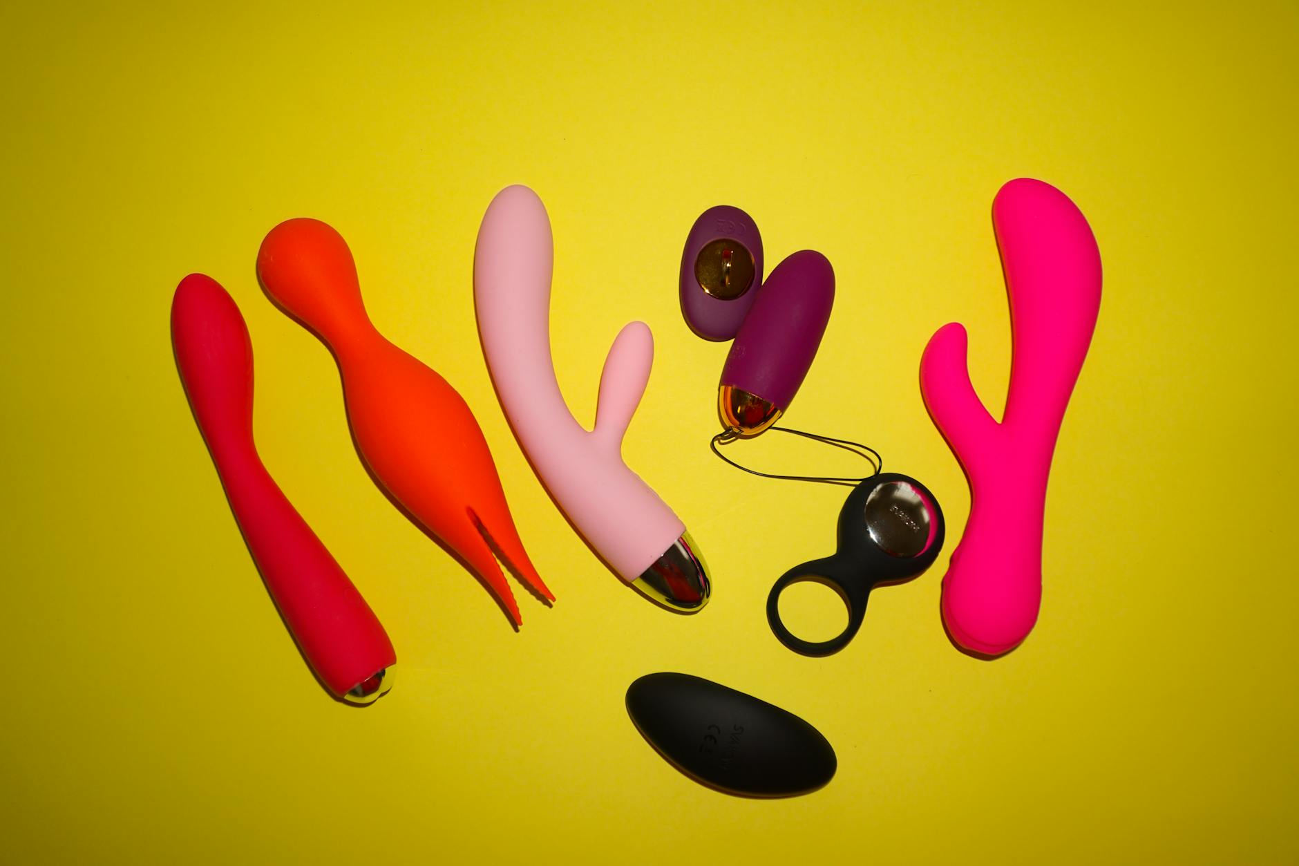 Woman holding silicone vibrators thoughtfully against neutral background